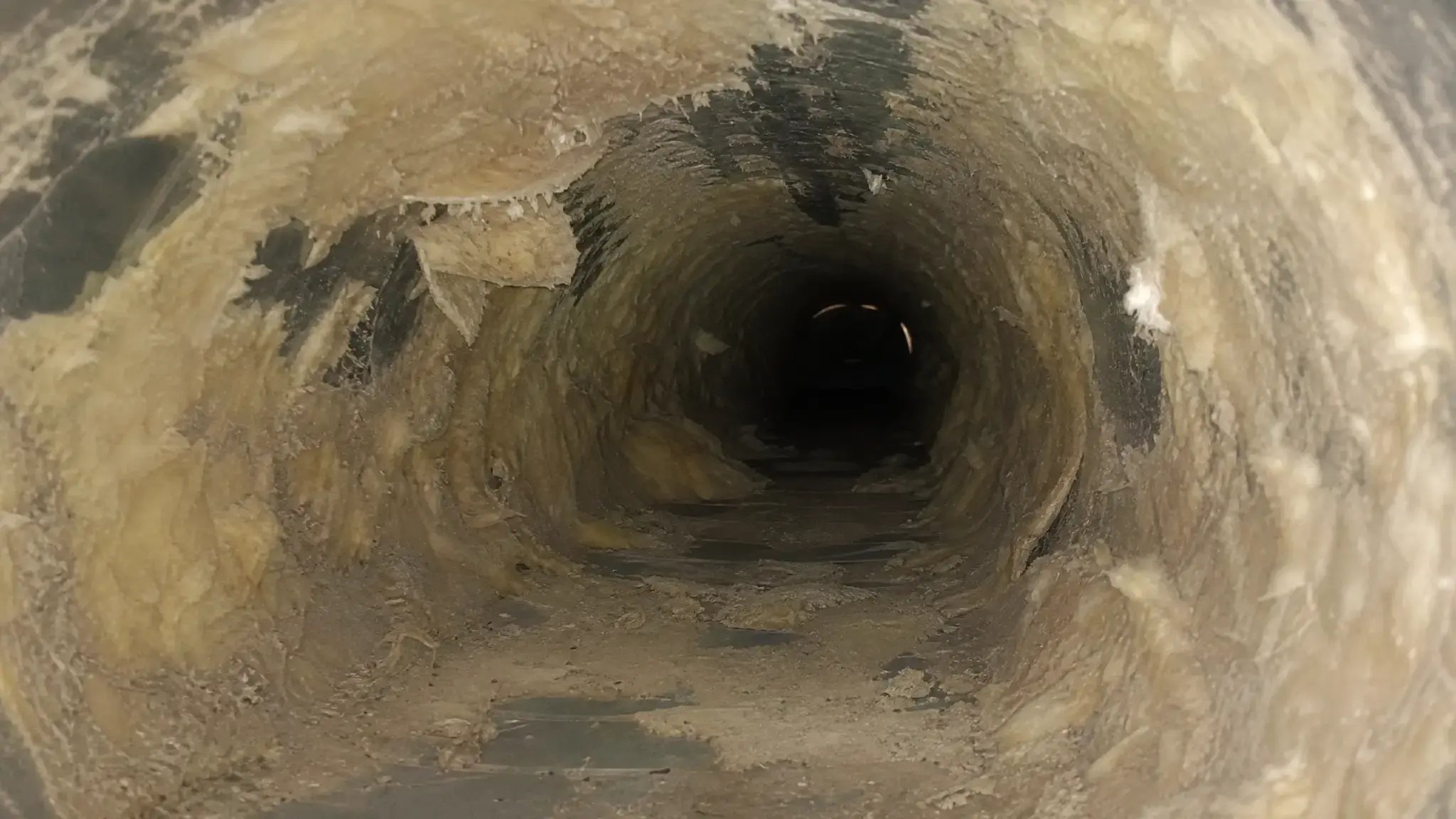 Close-up of deteriorating fiberglass duct liner inside a commercial HVAC system