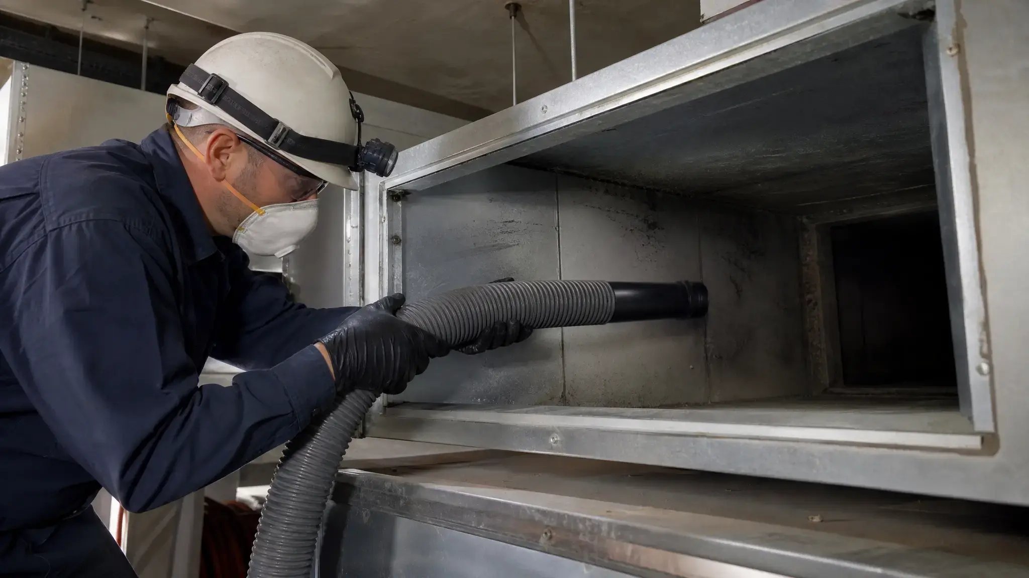NADCA-certified technician using HEPA vacuum to clean fiberglass-lined commercial ductwork