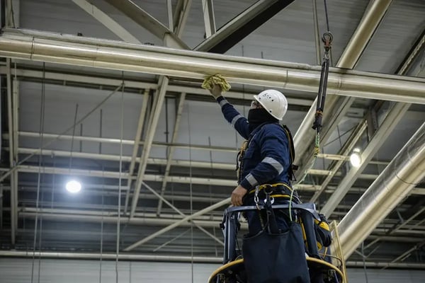 technician performing overhead cleaning on industrial facility structures