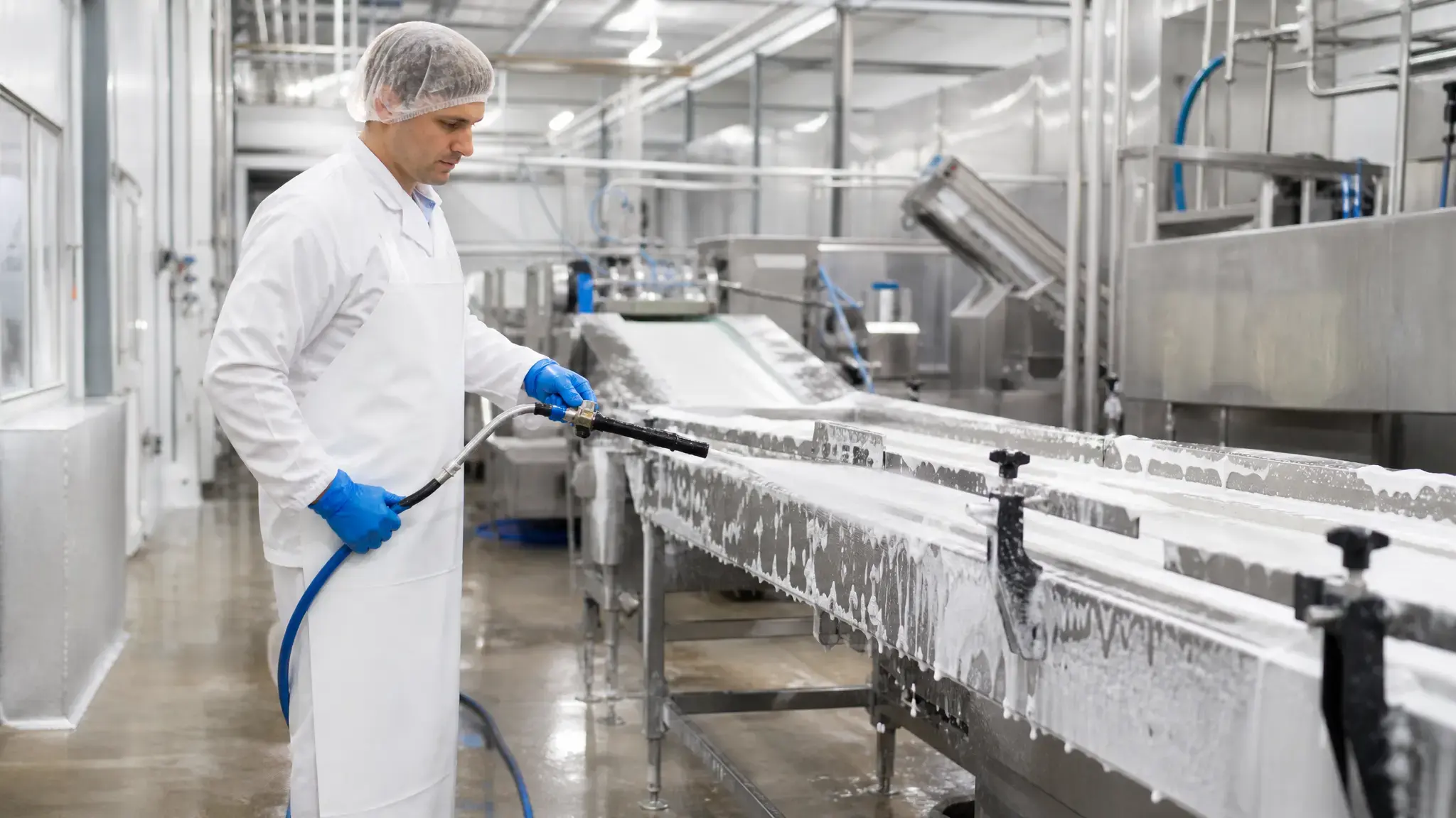 worker sanitizing stainless steel conveyor belt in food processing plant