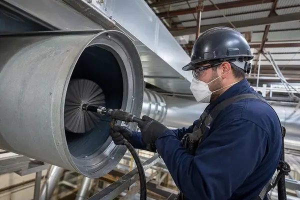 Technician inspecting large commercial air duct interior with inspection light