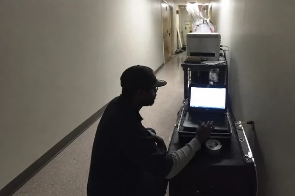 Technician monitoring an Aeroseal duct sealing machine from a laptop in a hallway