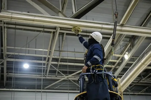 technician performing overhead cleaning on industrial facility structures