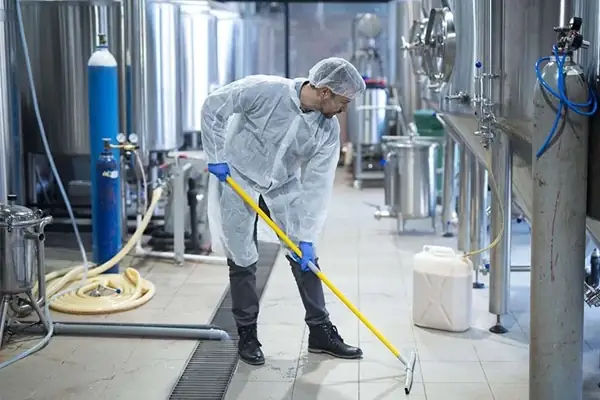 Worker in protective clothing mopping the floor of a stainless steel processing plant