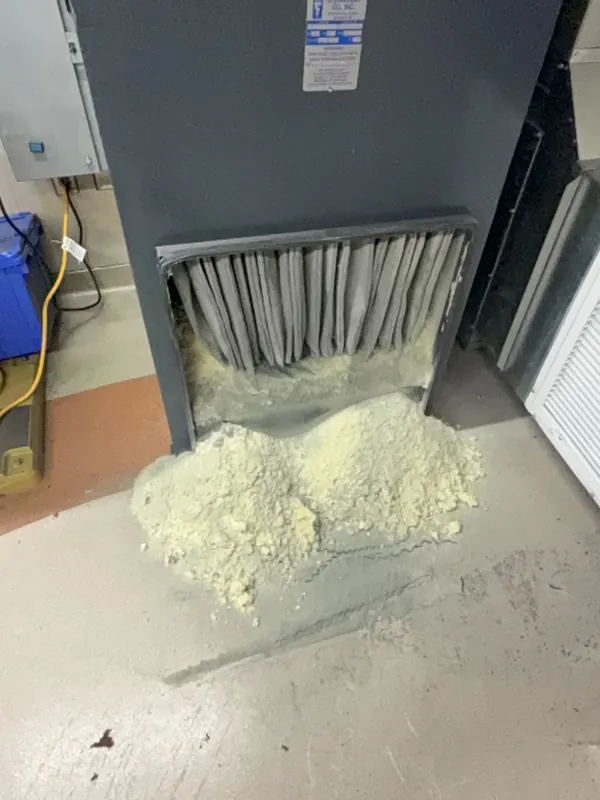 Before: air handler cabinet with packed filters and a pile of dust on the floor before Service-Tech air duct cleaning
