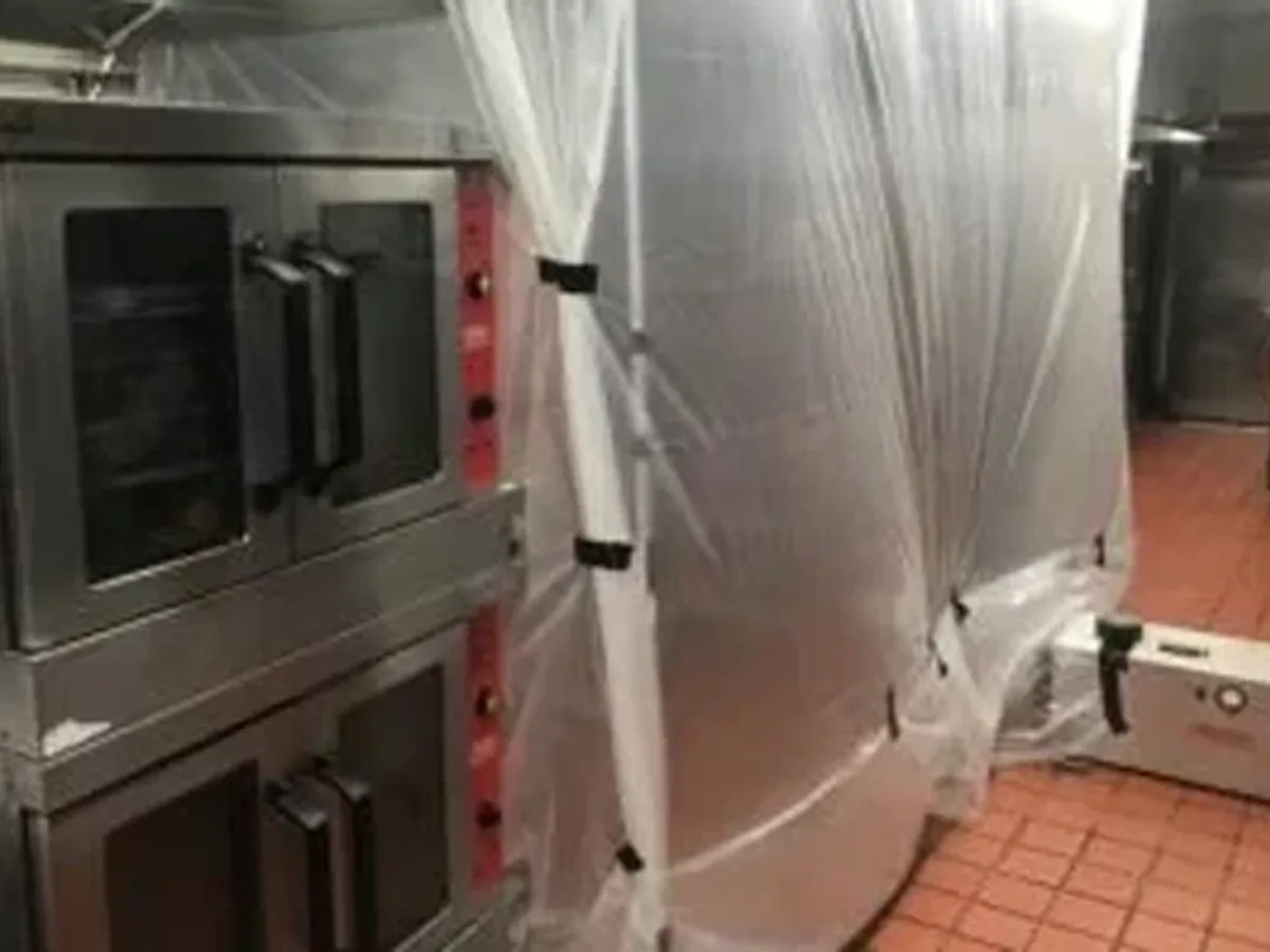 Plastic containment and an air scrubber set up around industrial ovens before cleaning