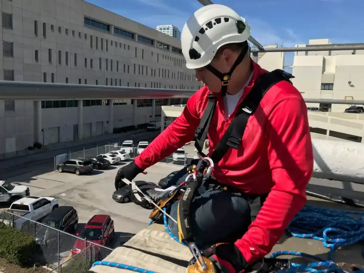 Service-Tech technician in a helmet and full-body harness tied off at a rooftop edge